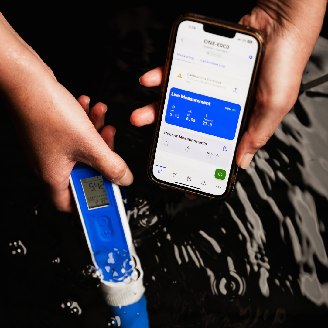 Person holding a water quality meter and a smartphone with an app displaying measurement results in water.