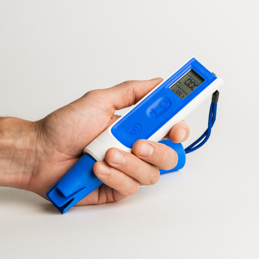 Hand holding a blue and white digital thermometer against a light background