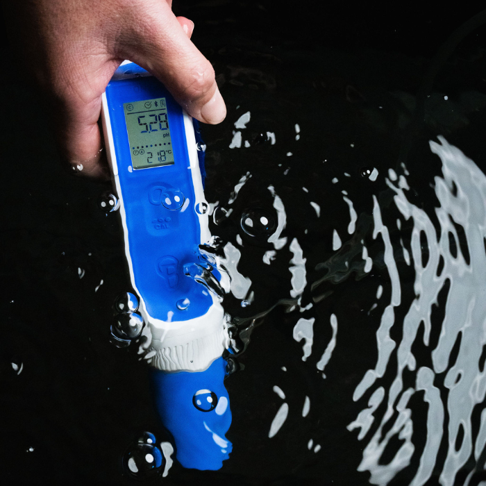 Hand holding a digital pH meter in water with splashes on a black background
