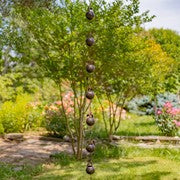 A hanging decorative garden ornament with multiple dark round weights suspended by strings from a tree in a landscaped garden.