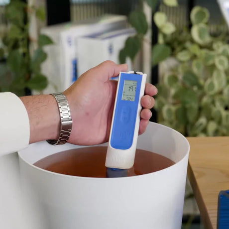 Hand holding a pH meter in a white container with a blurred background