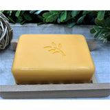 Yellow soap bar with a logo on a wooden soap dish against a natural background
