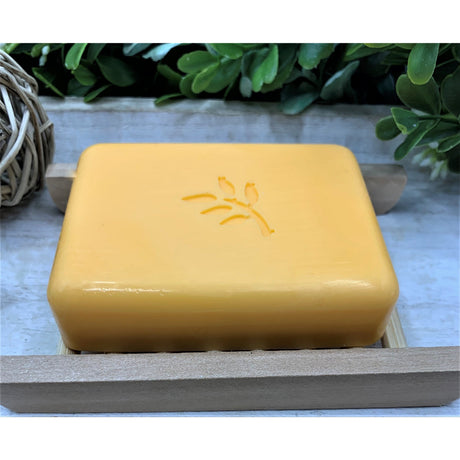 Yellow soap bar with a logo on a wooden soap dish against a natural background