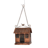 A hanging bird feeder shaped like a small rustic house, made of copper-toned metal with a chain and loop at the top, a small bird figure on the roof, and a feeder tray at the bottom, shown on a plain white background.