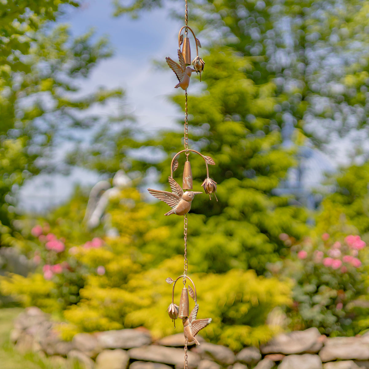 Decorative wind chime with hummingbird design against a garden background