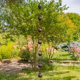 A hanging decorative garden ornament with multiple dark round weights suspended by strings from a tree in a landscaped garden.